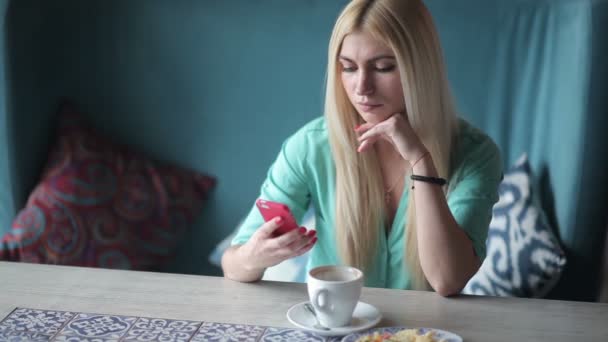 カフェで携帯電話を使用してコーヒー カップに青いシャツを着て若いブロンドの女性 — ストック動画