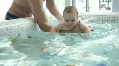 Slowmotion. Onun bebeği elele baba. Havuzda bebek. Bebek ve gülümseyen ve perplexedly etrafa yakışıklı strart su sıçramasına baba. Komik bebek başına yüzmeye çalışıyorum.