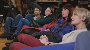 Genç insanlar komik performans ve gülmek bakıyor. Kadın ve erkek yastıklar katta oturuyor. Seyirciler onların önünde bir sahnede arıyorum. Genç rahatlatıcı insanlar ve iyi eğlenceler. İnsanlar için komik adam alkışlıyorum.