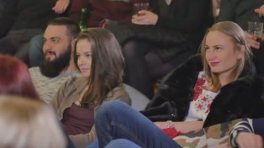 Gençler performans izliyor. Adam ve yastıklar katta oturan kadın. 