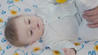 Yakın çekim. Küçük bebek bebek bezi üzerinde yatıyor. Sevimli çocuk el ve kafa farklı taraf hareket ediyor. Annenin elleri çocuğun bacakları hareket ediyor. Şirin bebek anne kamera dışında üzerinde görünüyor.