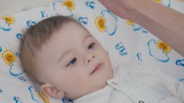 Yakın çekim. Sevimli bebek bebek bezi üzerinde bırakır. Annenin yavaş yavaş küçük oğlunun kafa dokunuşlar ver. Çocuk yapması. Anne küçük burun dokun. Çok güzel çocuk anne kamera dışında üzerinde görünüyor.
