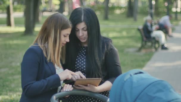 若い母親とかなり女性は公園に立って タブレットを使用します 人の友人の話といくつかの情報を話し合います ハンサムな男は 女性と彼らと抱擁します タブレットと協議を使用して若者 — ストック動画