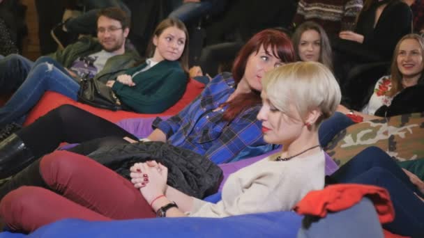 年轻人看喜剧表演和微笑 男人和女人坐在地板上的枕头 — 图库视频影像