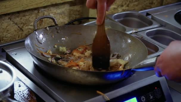 Шеф-повар смешивает рисовую лапшу и жареные овощи с лопаткой в горячей сковороде — стоковое видео