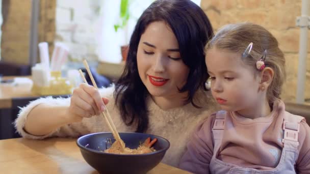 Ung mamma mata hennes lilla dotter med en koreanska nudlar i restaurang — Stockvideo