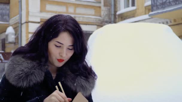 年轻的韩国在下雪的时候在街上吃面条。 — 图库视频影像