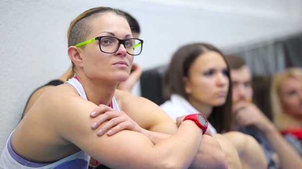 Mujer joven en gafas escuchando a un entrenador en el entrenamiento en el gimnasio — Vídeo de stock