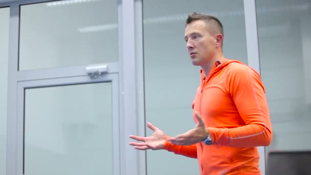 De trainer in oranje kostuum in gesprek met het publiek over de opleiding — Stockvideo