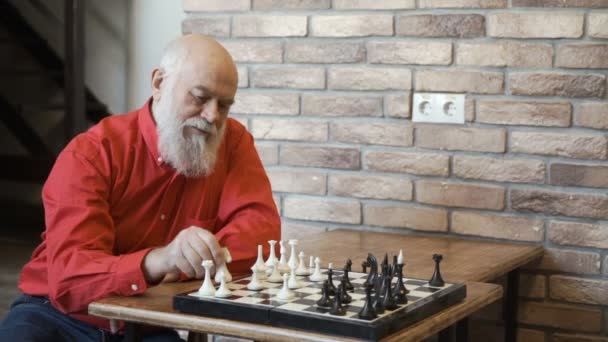 Седовласый мужчина играет в шахматы сам с собой — стоковое видео