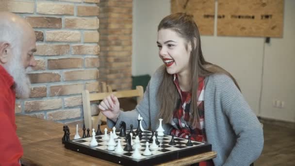 Молодая красивая девушка играет в шахматы с дедушкой — стоковое видео