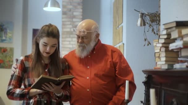 Joven chica bonita lee interesante libro junto con el abuelo — Vídeos de Stock