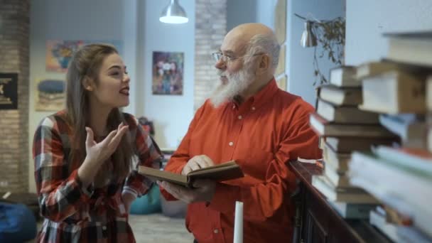 Молодая девушка обсуждает книгу с дедушкой — стоковое видео