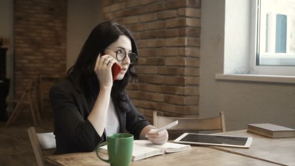 Elegante donna in occhiali parla al telefono seduto al tavolo in ufficio — Video Stock