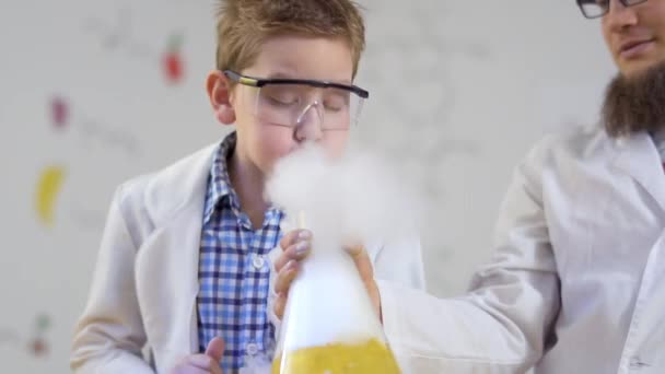 Little boy blows at steaming yellow liquid — Stock Video