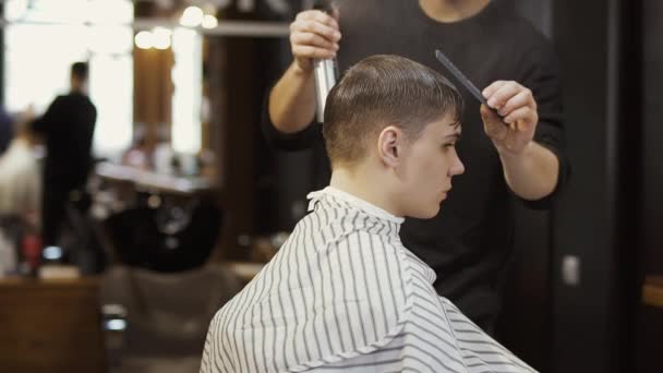 Профессиональный парикмахер делает стильную стрижку для молодого парня — стоковое видео