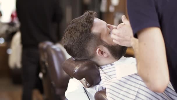 Stylist snijdt baard tot volwassen man met elektrisch scheerapparaat — Stockvideo