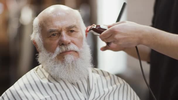 Stylist makes modern hairstyle for mature man with electric razor — Stock Video