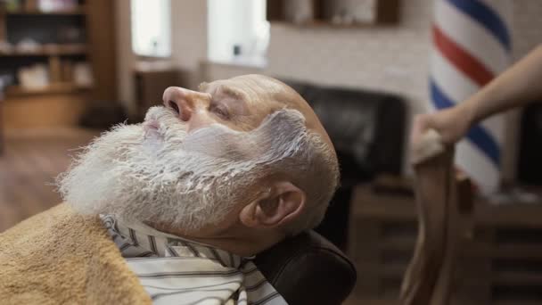 Peluquero cubre la cara del hombre maduro con una toalla caliente — Vídeo de stock