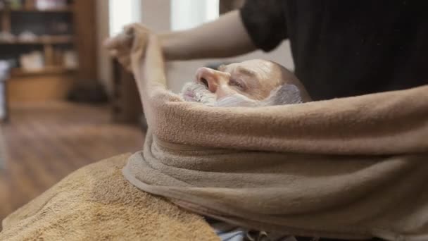 Barbiere copre il viso di uomo maturo con un asciugamano caldo prima di radersi la barba — Video Stock