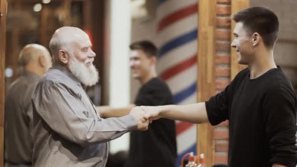 Счастливый зрелый мужчина пожимает руку парикмахеру и благодарит его за работу — стоковое видео
