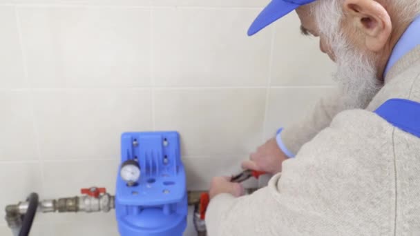 Trabajador de pelo gris desenrolla tuerca en la tubería de calefacción — Vídeos de Stock