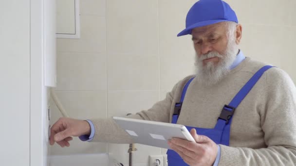 Volwassen grijs-haired werknemer past de temperatuur op de ketel — Stockvideo