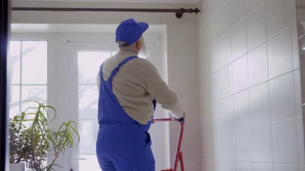 Hombre mayor con monos protectores azules reparando cornisa sobre la ventana — Vídeos de Stock