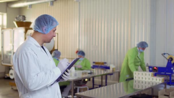 Головний інженер спостерігає за роботою жінок на заводі і робить нотатки у звіті — стокове відео