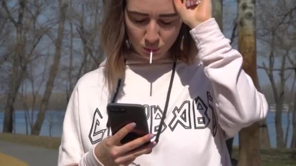 Fille avec message sucette avec des amis et se tient dans le parc avec planche à roulettes — Video