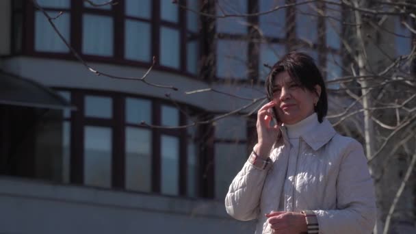 Wanita senior berbicara di telepon di latar belakang gedung kantor — Stok Video