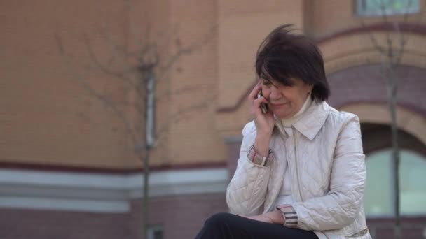 Abuela habla por teléfono en el fondo del edificio de oficinas — Vídeo de stock