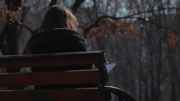 Молодая девушка с блокнотом отдыхает на скамейке в парке — стоковое видео