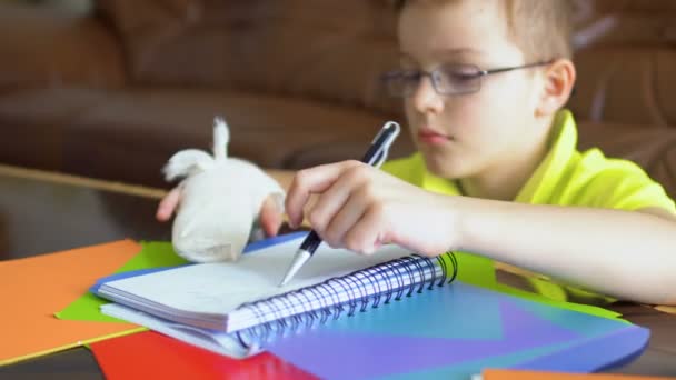 Jongen het dragen van bril en met gebroken hand proberen te maken van huiswerk met linkerhand — Stockvideo