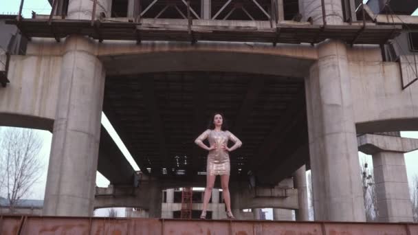 Красивая брюнетка в платье стоит на фоне заброшенного моста — стоковое видео