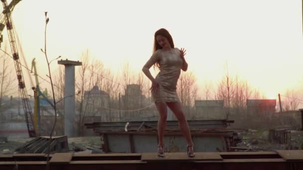 Красива жінка танцює на заході сонця, стоячи на металевому будівництві — стокове відео