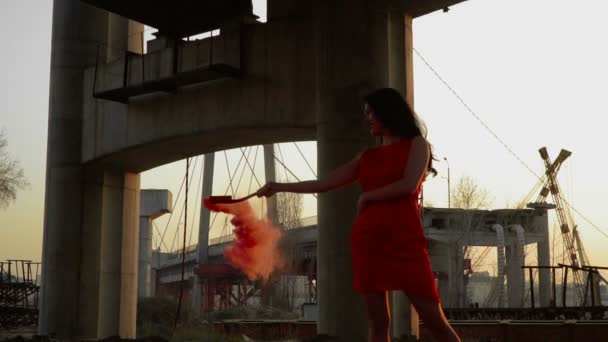 Piękna kobieta nosi czerwona sukienka taniec o zachodzie słońca pod mostem opuszczonym — Wideo stockowe
