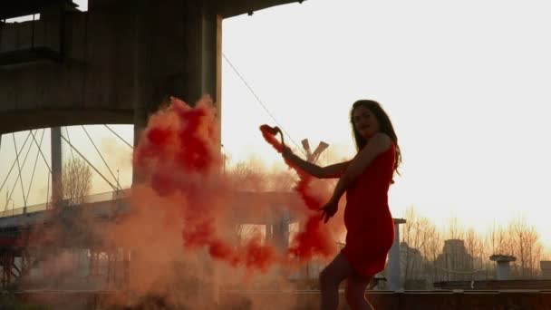 Prachtige vrouw met rode rook flare dansen onder verlaten brug — Stockvideo