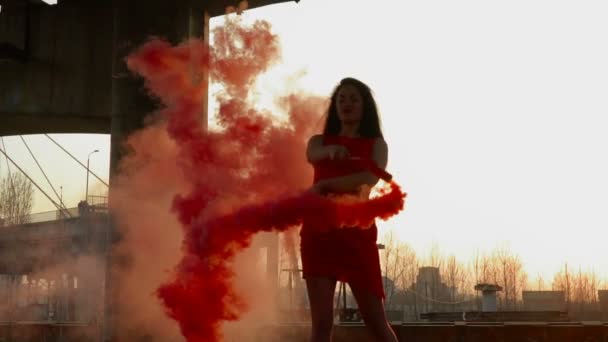 Κομψή γυναίκα με κόκκινο φόρεμα χορό με κόκκινο καπνός κοντά εγκαταλειφθεί γέφυρα — Αρχείο Βίντεο