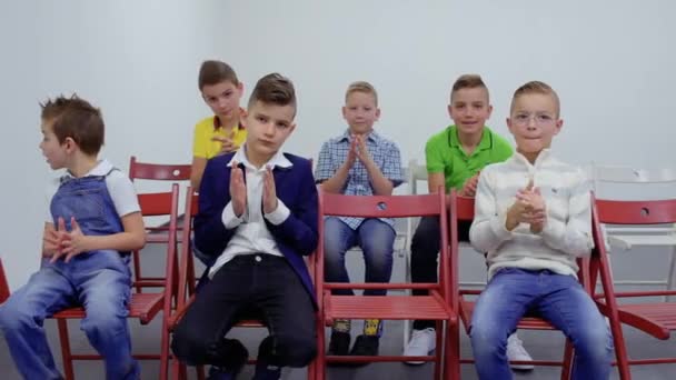Милые кавказские мальчики сидят за стульями и аплодируют — стоковое видео
