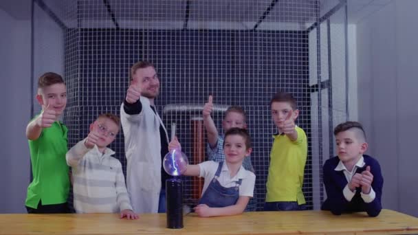 Kinderen en leraar toont duimen omhoog houdt glazen globe over Tesla coil — Stockvideo