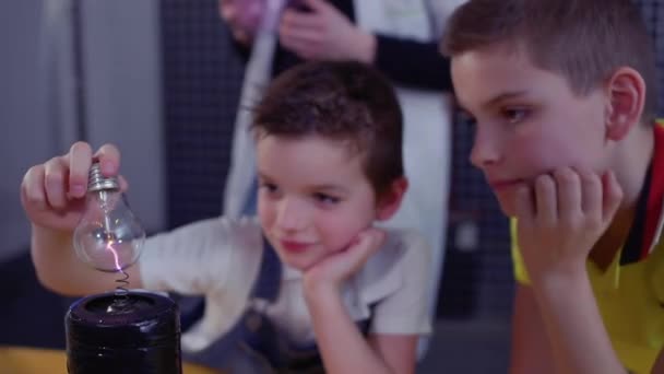 Niños relojes para el relámpago dentro de la lámpara eléctrica que lo sostiene sobre la bobina Tesla — Vídeo de stock