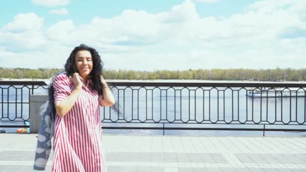 Hermosa morena en vestido está caminando en el terraplén cerca del río — Vídeo de stock