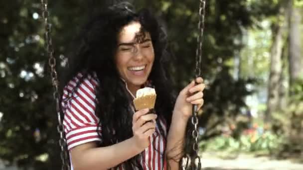 Красива брюнетка їсть морозиво на гойдалці в парку — стокове відео