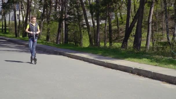 少年は、スローモーションで夏の公園でのキック スクーターに乗っています。 — ストック動画