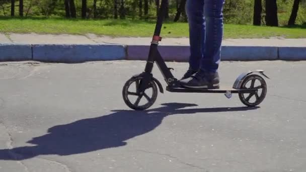Pojke kick bär jeans och sneakers ridning på scooter på vägen — Stockvideo