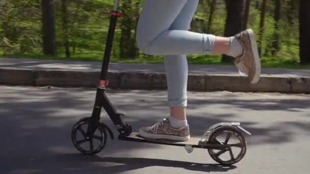 Mulher adulta monta em chute scooter perto das crianças em patins no parque — Vídeo de Stock