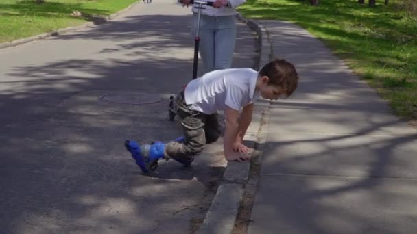 Chlapeček na kolečkových bruslích zvedá na nohy po pádu na asfalt — Stock video