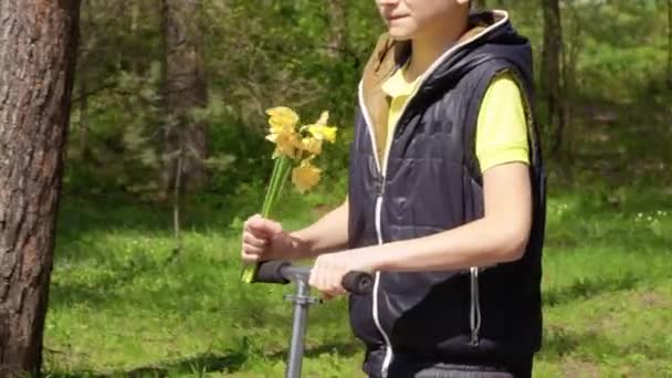 Pojke bär narcissus för hans mor ridning på kick scooter — Stockvideo