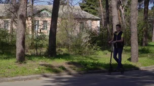 El niño monta en patinete scooter en el parque en cámara lenta — Vídeo de stock